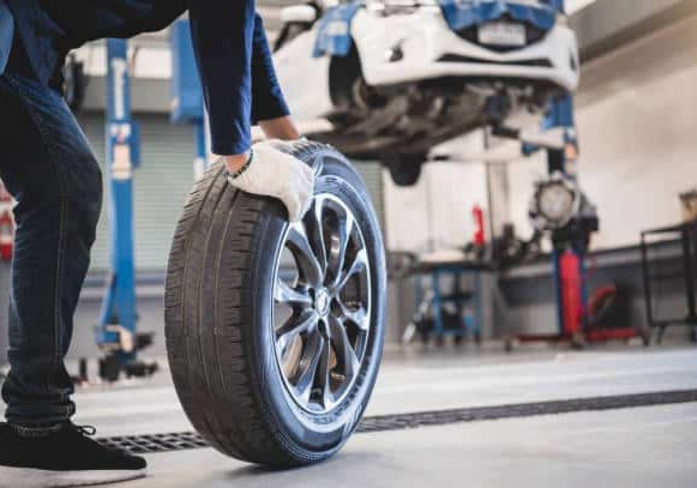 Male mechanic hold and rolling tire at repairing service garage background. Technician man replacing winter and summer tyre for safety road trip. Transportation and automotive maintenance concept